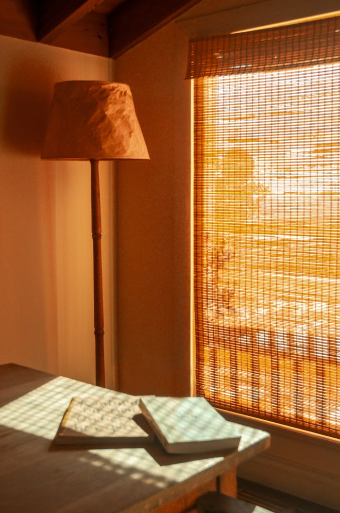 Room interior with textbooks on table against floor lamp and wicker curtain in house on sunny day