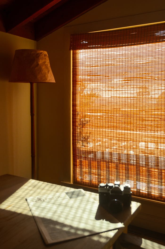Vintage photo camera on newspaper on desk against lamp and straw curtain at home in sunlight
